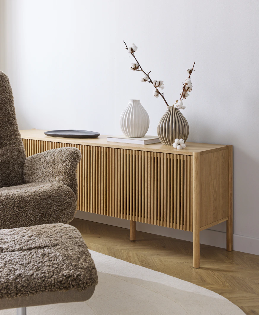 En tv-bänk med ribbad front i ljust trä står framför en vit vägg.