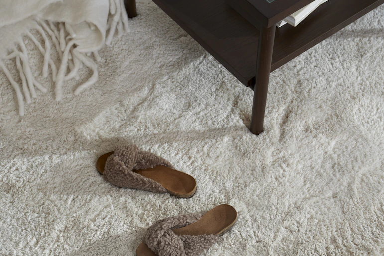 Ett par tofflor och ett mörkt soffbord står på en vit matta.