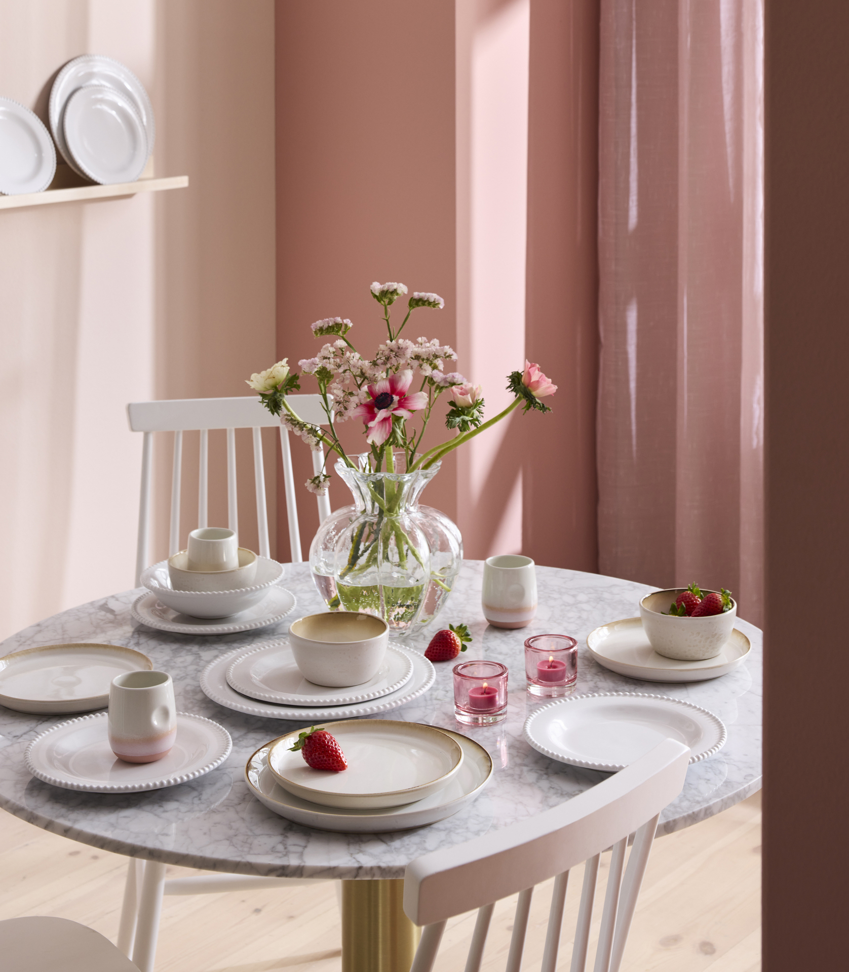 I ett rosa matrum står ett bord med ljus bordsskiva i marmor som är dukat med ljust porslin i olika sorter.