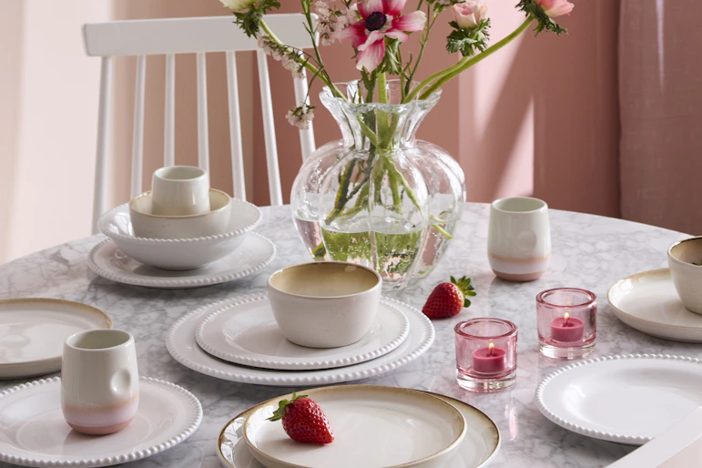 I ett rosa matrum står ett bord med ljus bordsskiva i marmor som är dukat med ljust porslin i olika sorter.