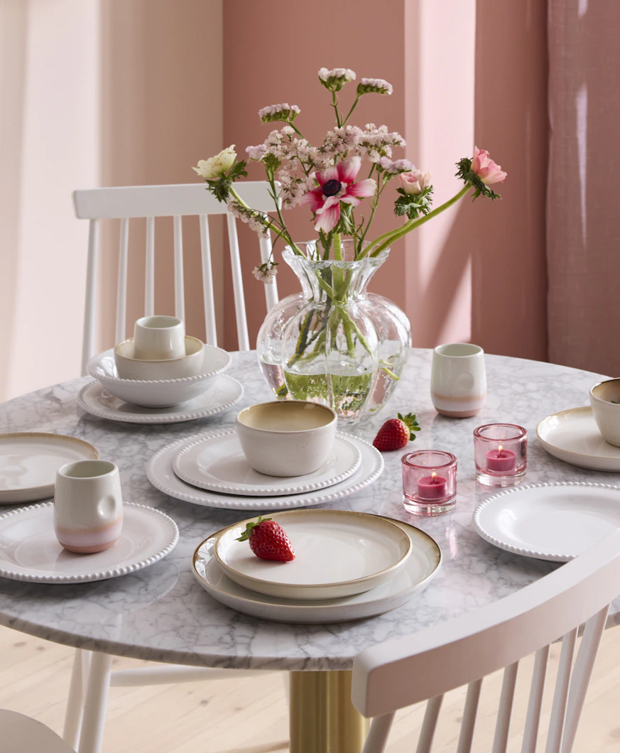 I ett rosa matrum står ett bord med ljus bordsskiva i marmor som är dukat med ljust porslin i olika sorter.