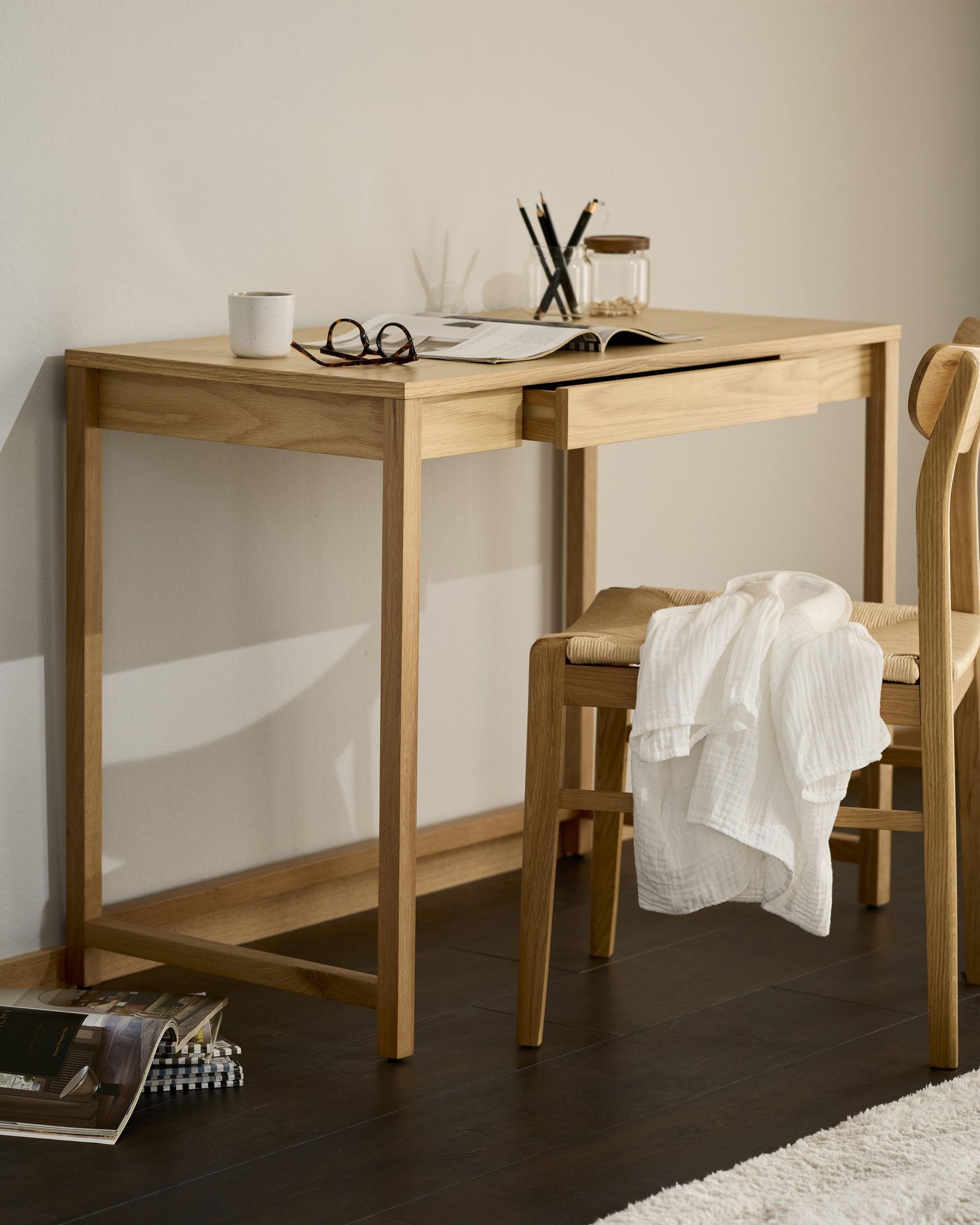 Ett skrivbord i ljust trä och matchande stol står framför en ljus vägg.