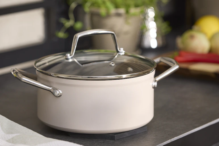 En beige kastrull med lock står på en spis.