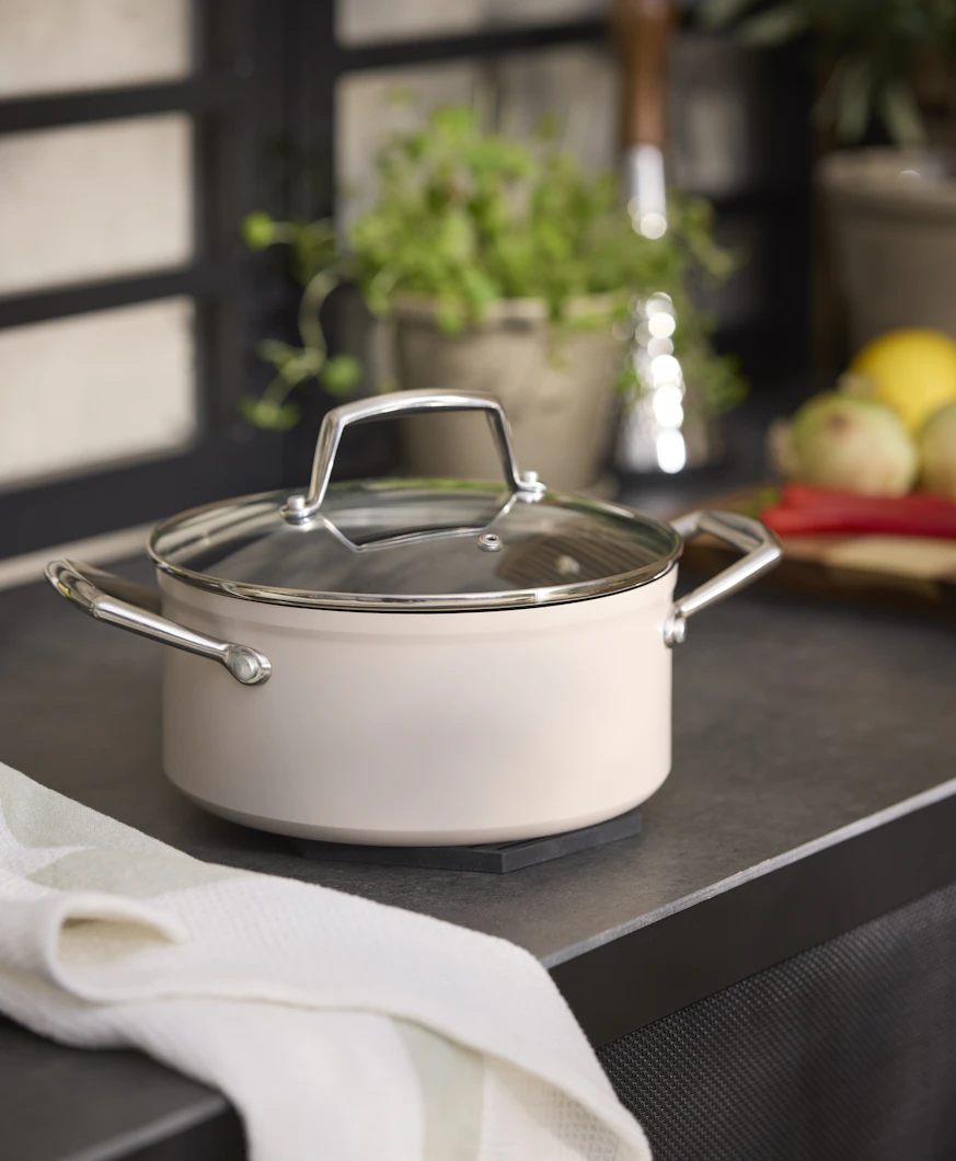 En beige kastrull med lock står på en spis.