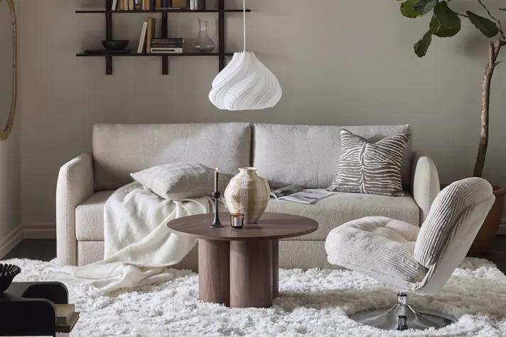 En beige bäddsoffa med raka linjer står i ett vardagsrum inrett i neutrala toner