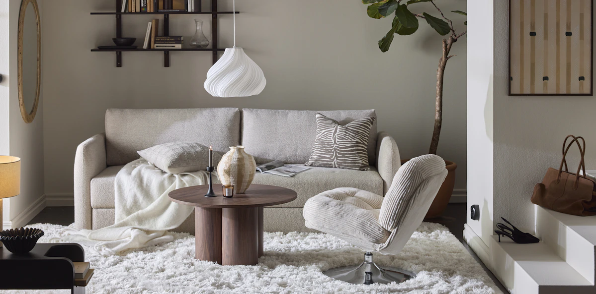 En beige bäddsoffa med raka linjer står i ett vardagsrum inrett i neutrala toner