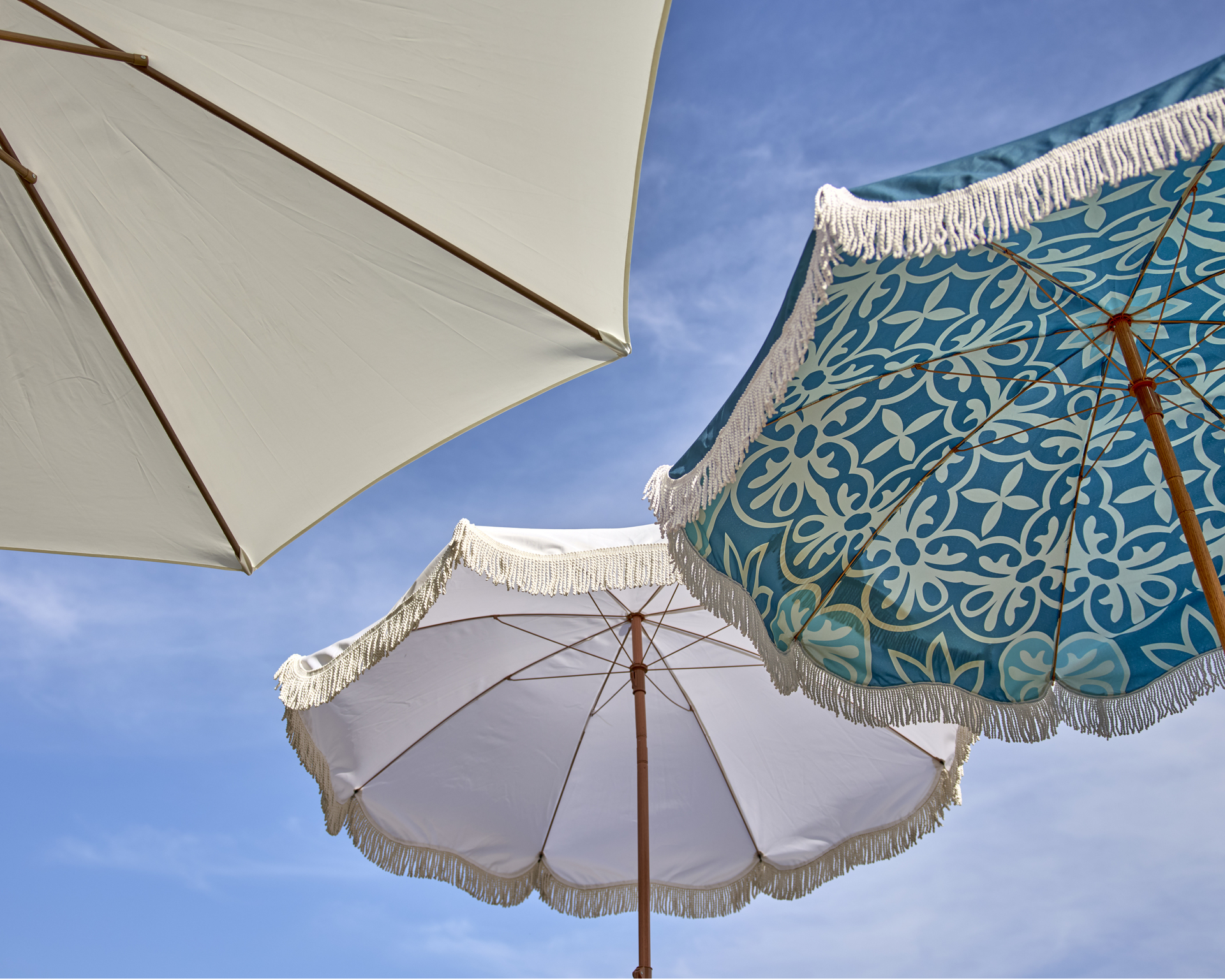 Tre parasoll med en klarblå himmel som bakgrund, två är vita och ett är mönstrat. 
