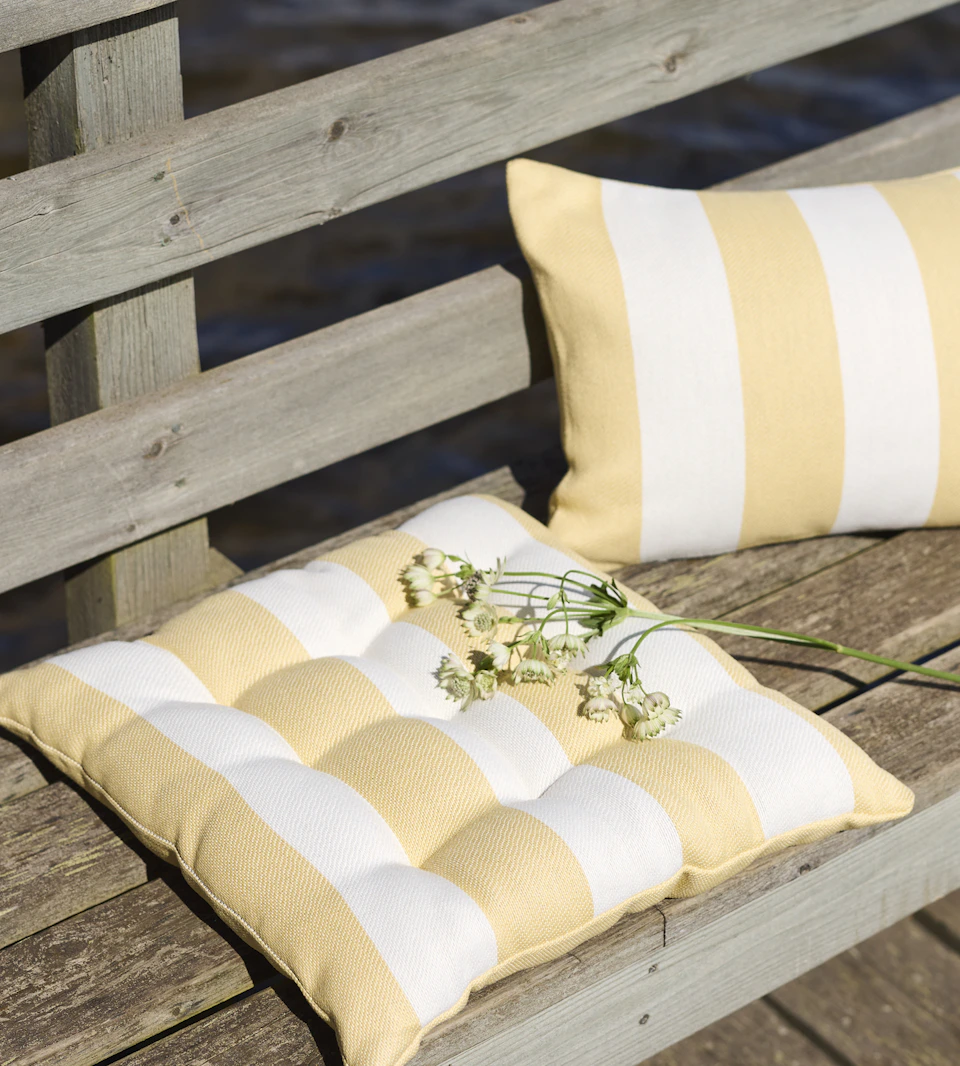 en dyna och kudde med gula och vita ränder ligger på en bänk utomhus