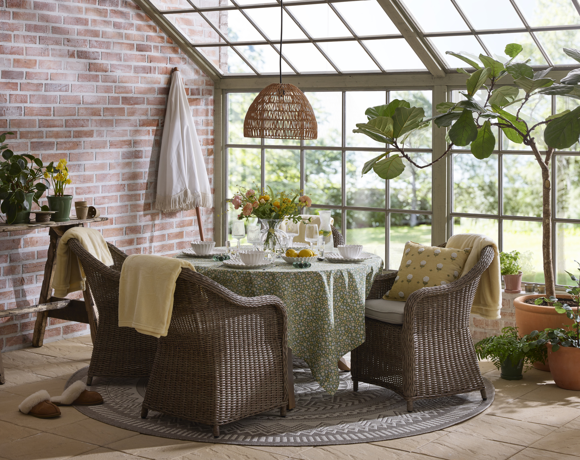 En utesoffgrupp med runt bord och fyra fåtöljer i konstrotting står i ett orangeri fyllt av växter.