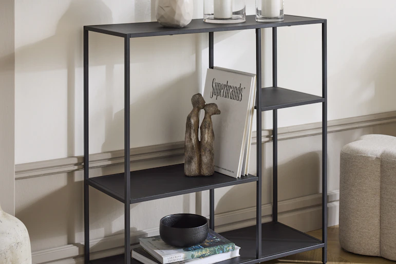 en svart hylla med olika dekorationer står framför en vit vägg