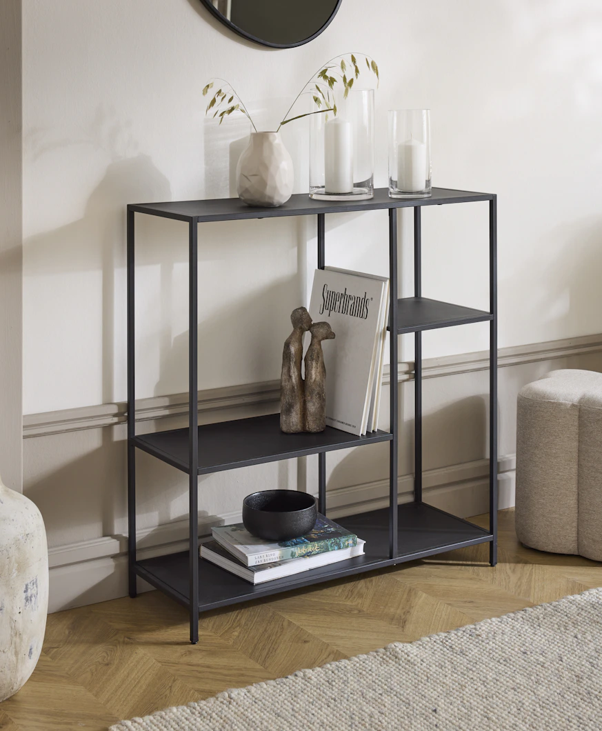 en svart hylla med olika dekorationer står framför en vit vägg