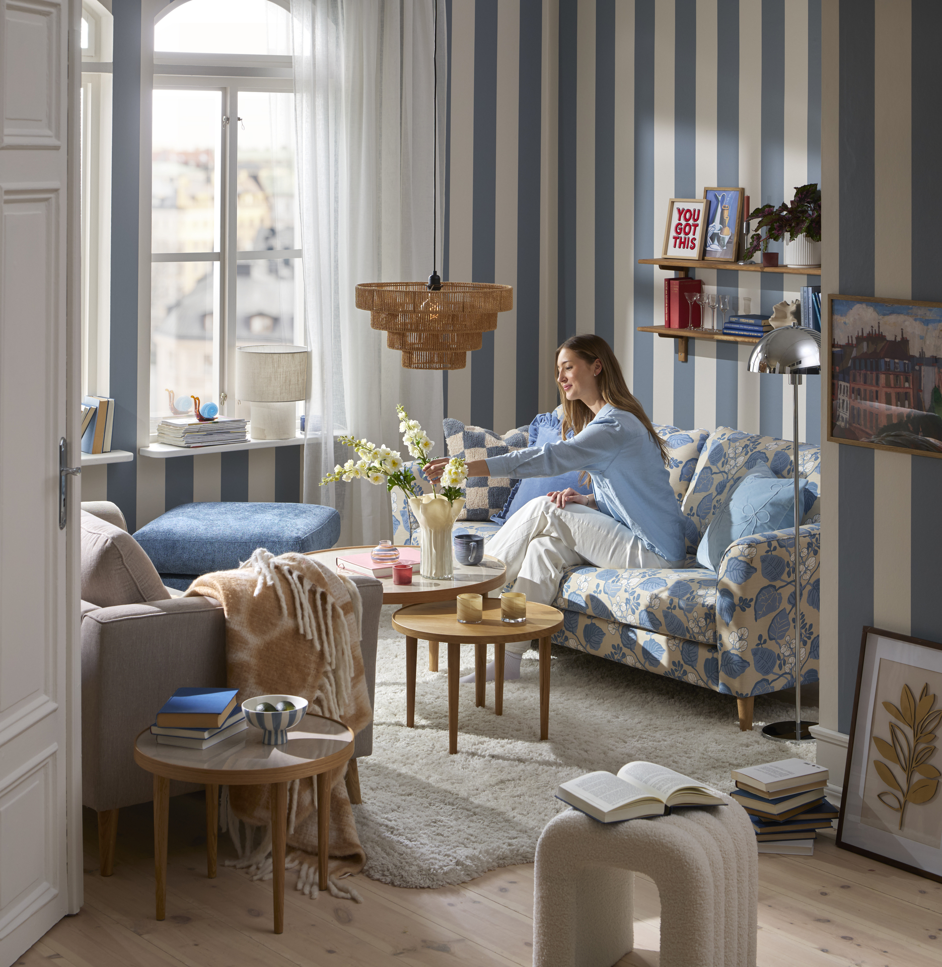 I ett lekfullt inrett vardagsrum med blåvit randig tapet sitter en ung kvinna i en blåmönstrad soffa.