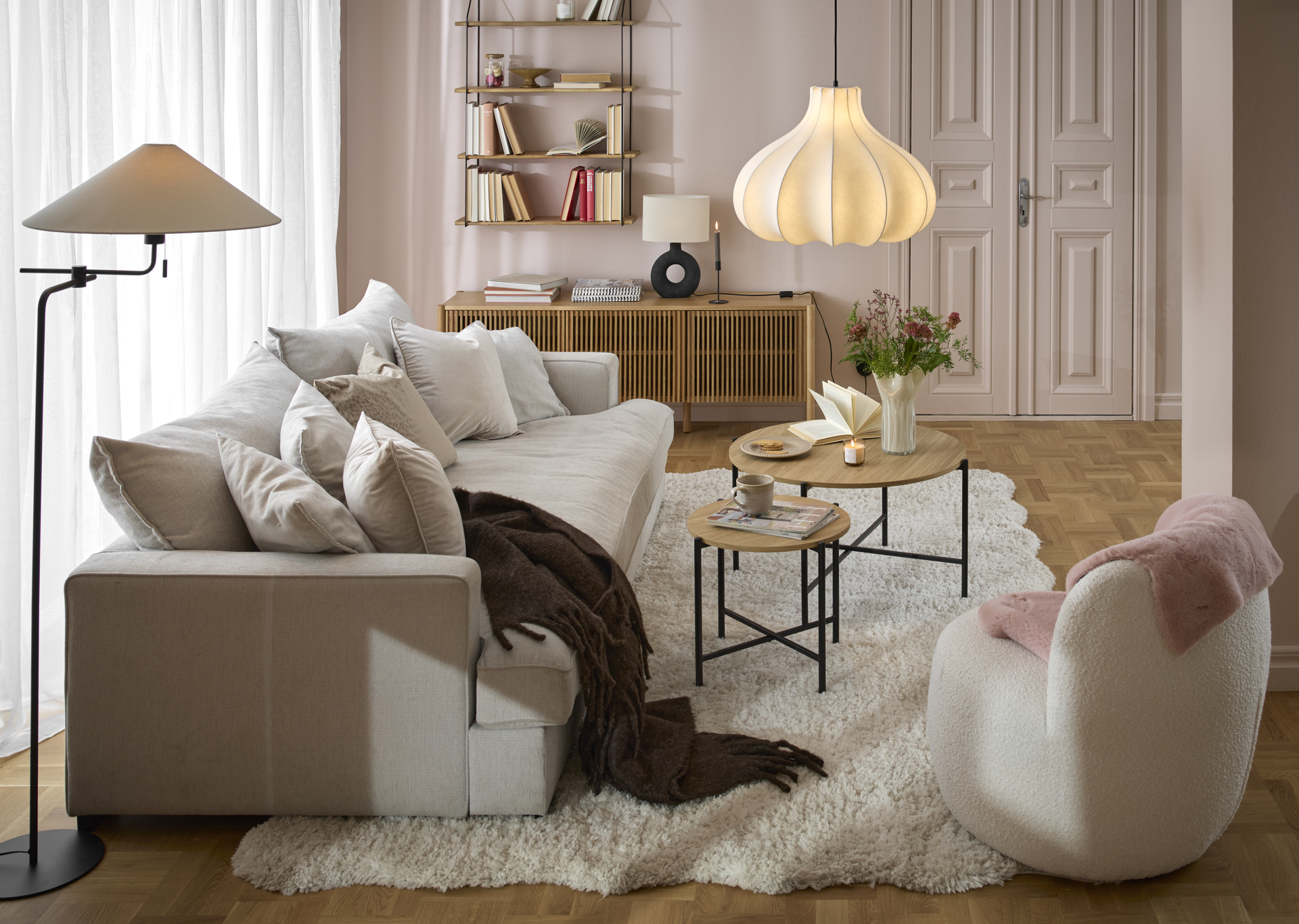 I ett rosa vardagsrum står en beige, djup soffa framför ett stort fönsterparti