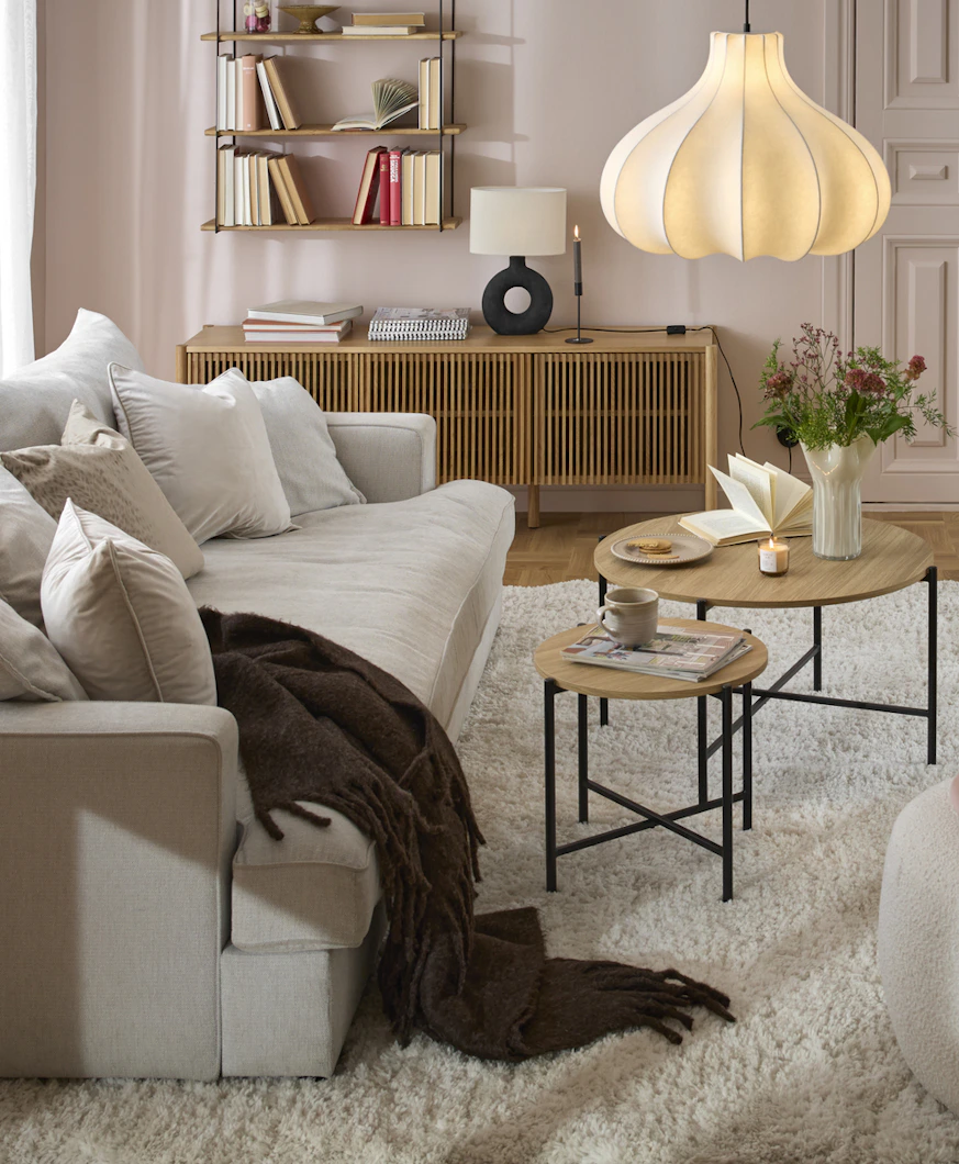 I ett rosa vardagsrum står en beige, djup soffa framför ett stort fönsterparti