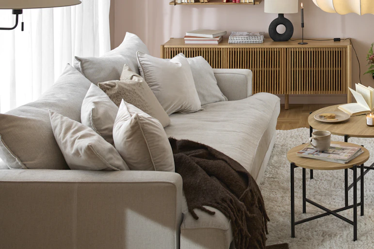 I ett rosa vardagsrum står en beige, djup soffa framför ett stort fönsterparti