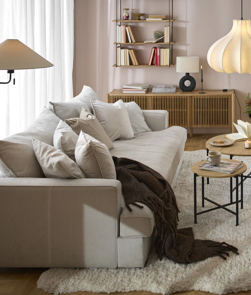 I ett rosa vardagsrum står en beige, djup soffa framför ett stort fönsterparti