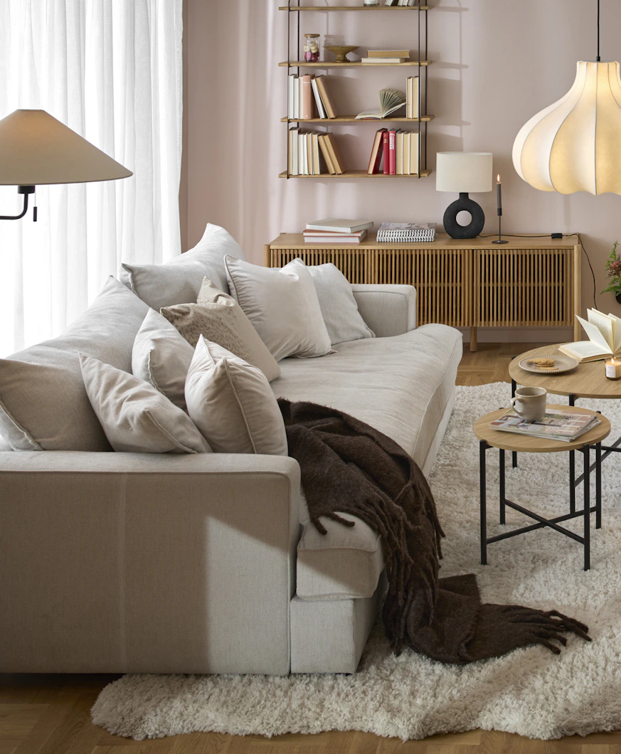 I ett rosa vardagsrum står en beige, djup soffa framför ett stort fönsterparti