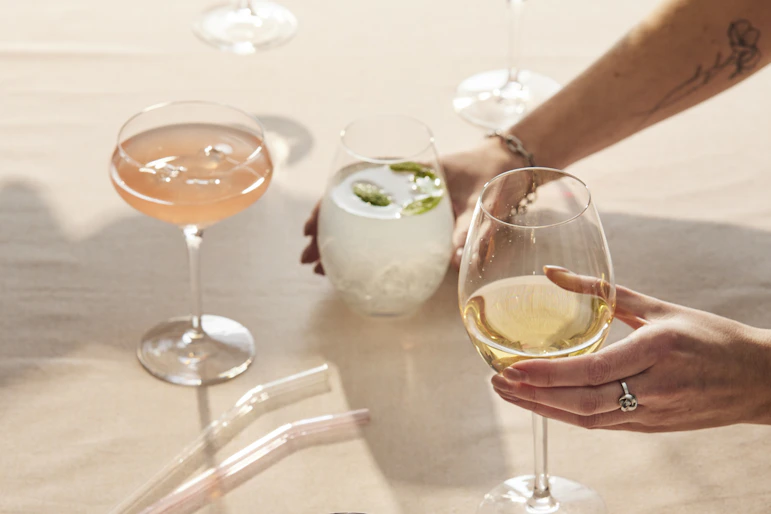 Flera händer stäcker sig över ett bord och skålar i glas fyllda med olika sorters drinkar