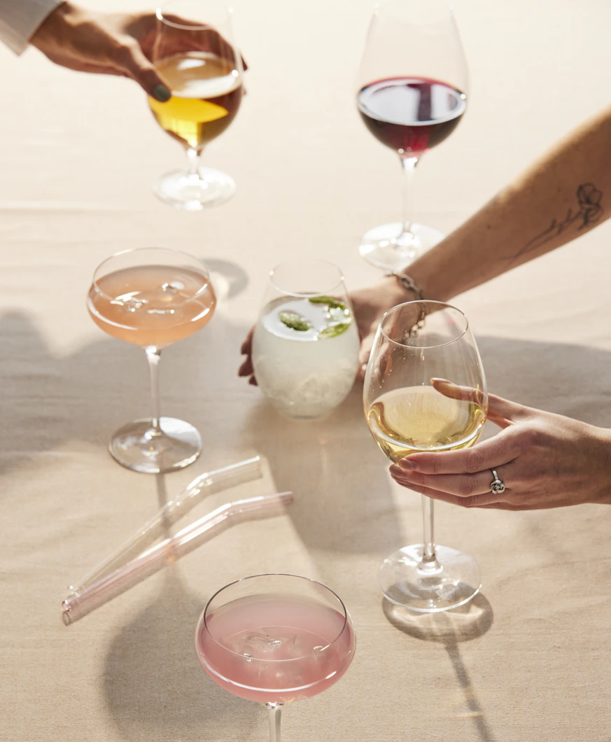 Flera händer stäcker sig över ett bord och skålar i glas fyllda med olika sorters drinkar