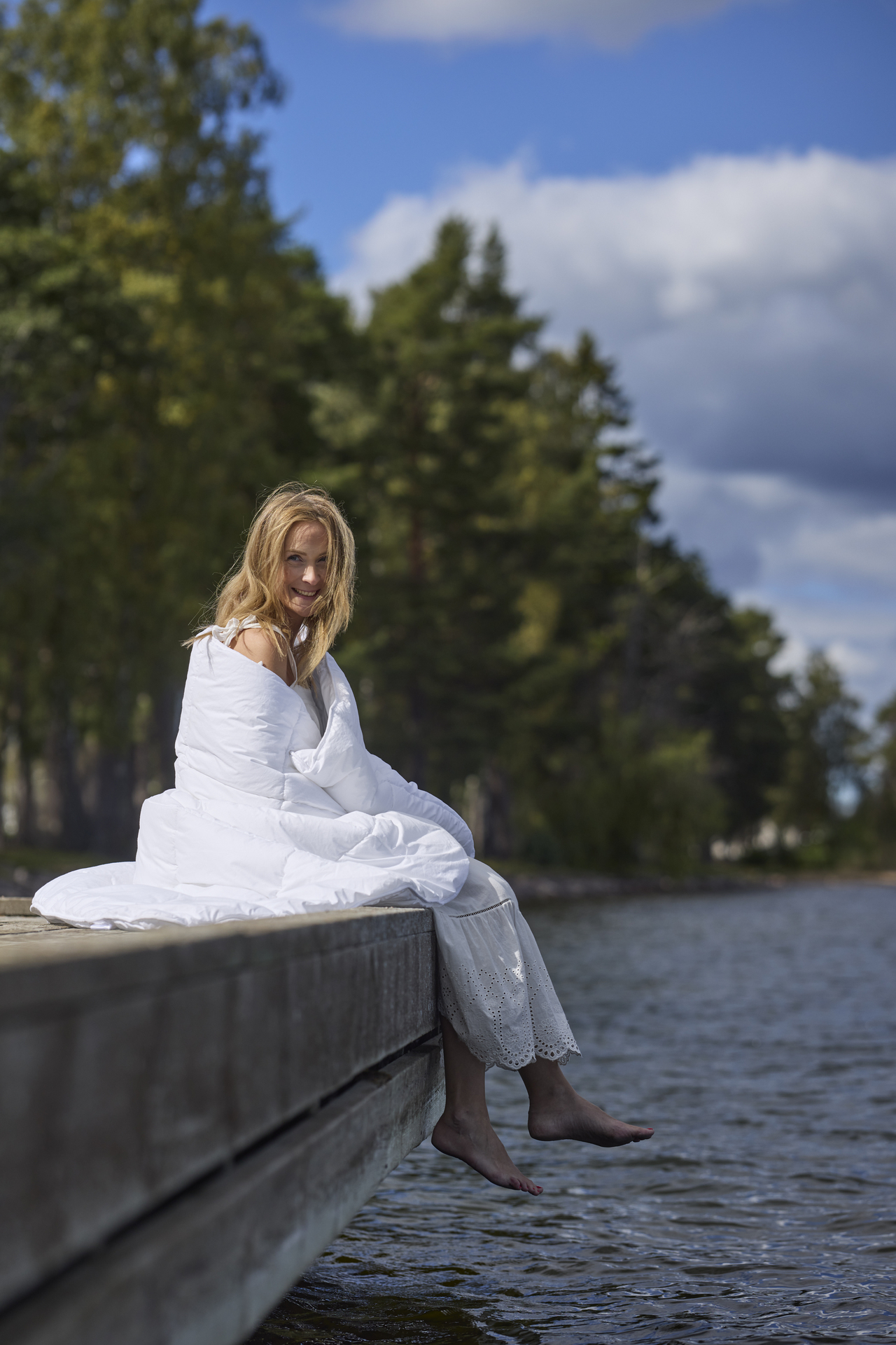 På en brygga sitter en kvinna inlindad i ett fluffigt täcke