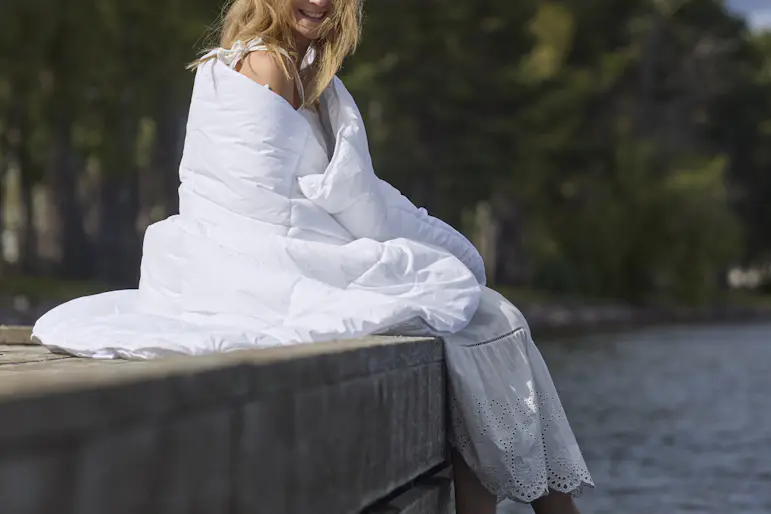 På en brygga sitter en kvinna inlindad i ett fluffigt täcke