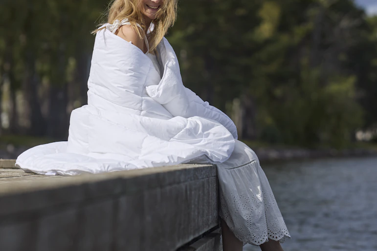 På en brygga sitter en kvinna inlindad i ett fluffigt täcke