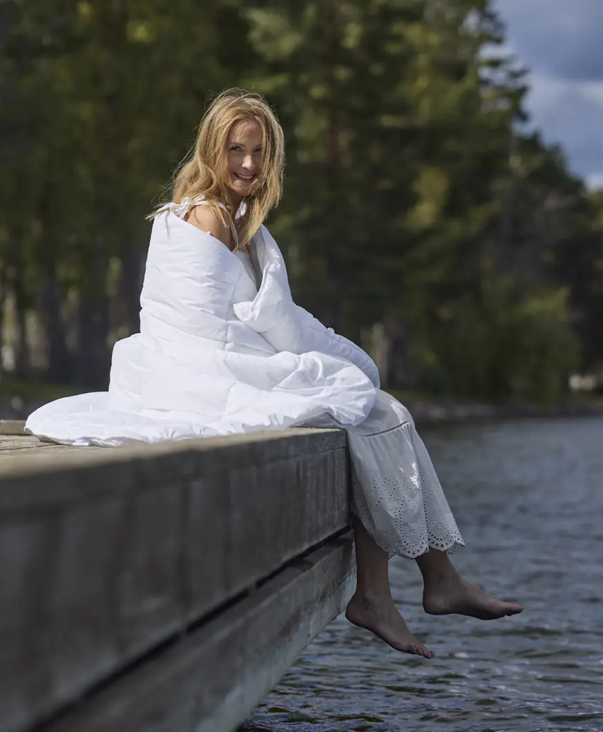 På en brygga sitter en kvinna inlindad i ett fluffigt täcke