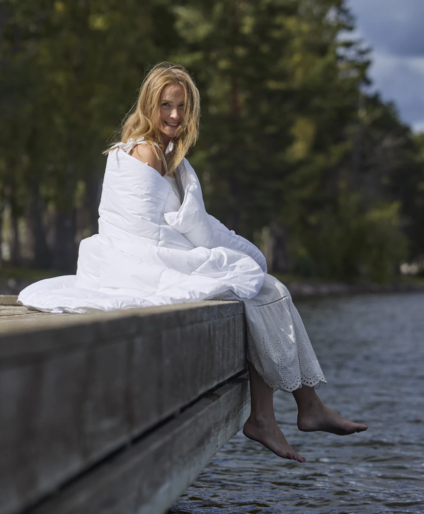 På en brygga sitter en kvinna inlindad i ett fluffigt täcke