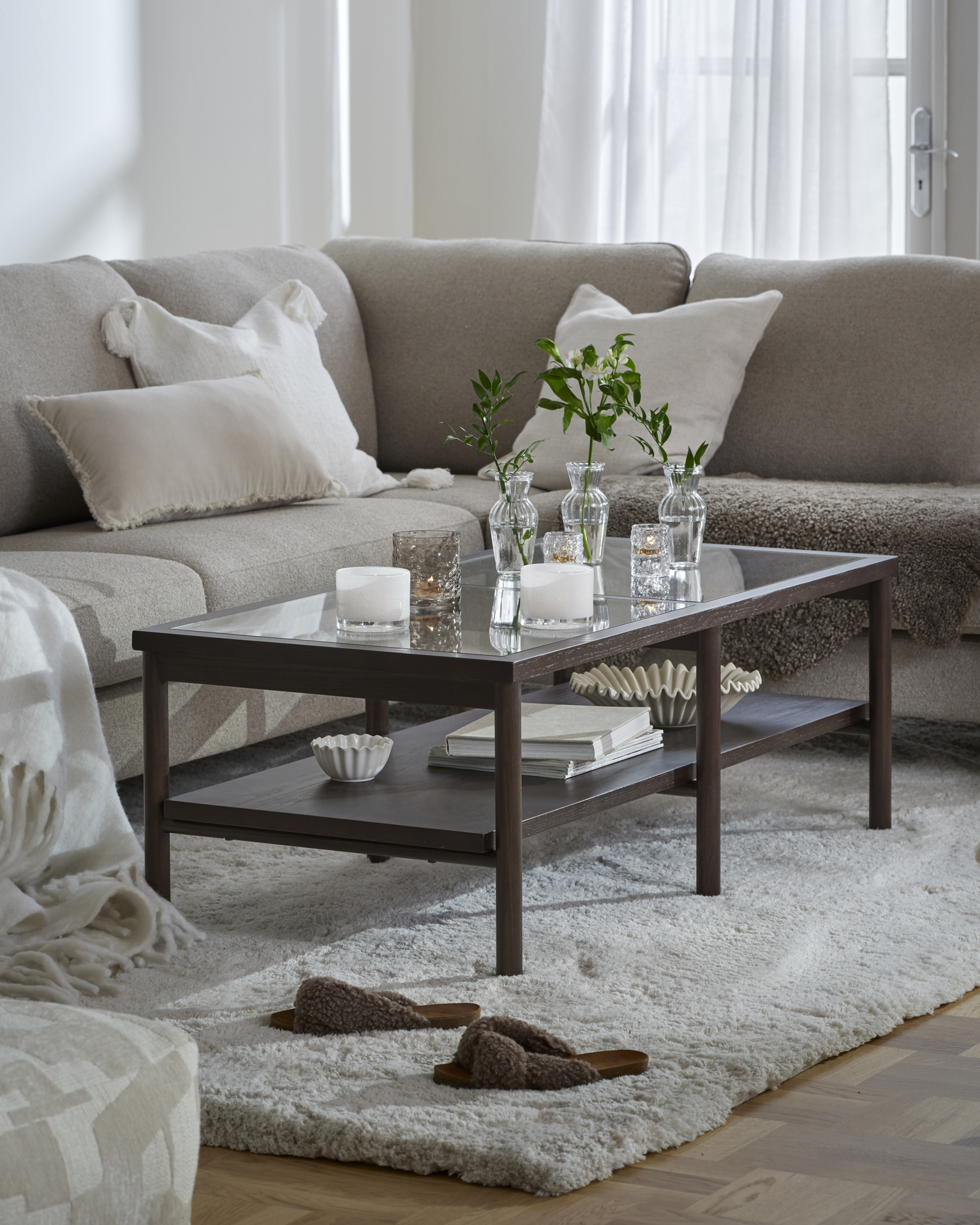 Framför en beige soffa står ett stilrent soffbord i mörkt trä och glas