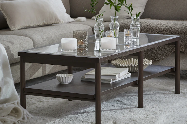 Framför en beige soffa står ett stilrent soffbord i mörkt trä och glas
