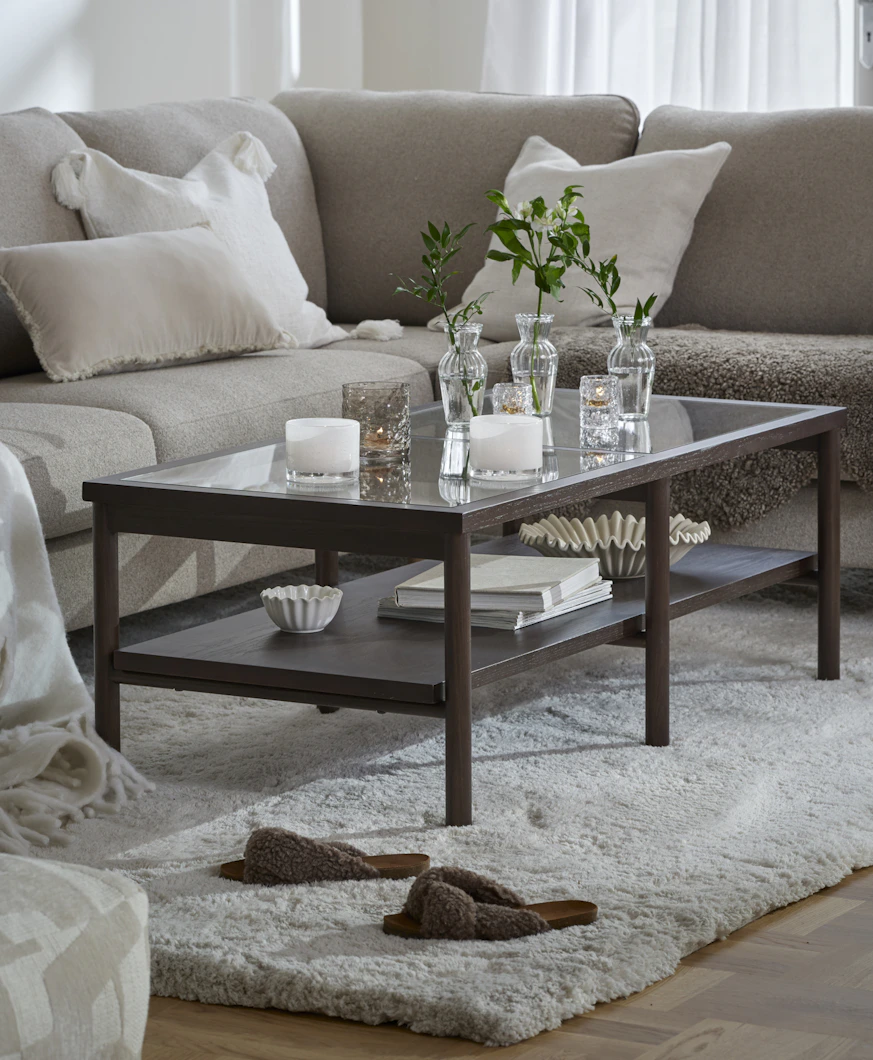 Framför en beige soffa står ett stilrent soffbord i mörkt trä och glas