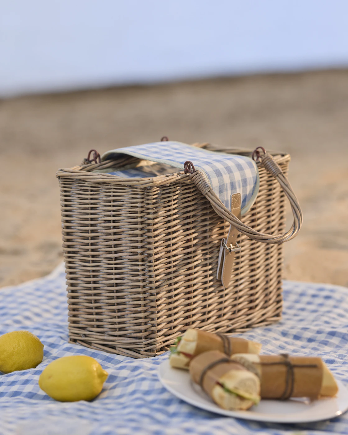 En picknickkorg står på en rutig filt tillsammans med en tallrik mat och citroner