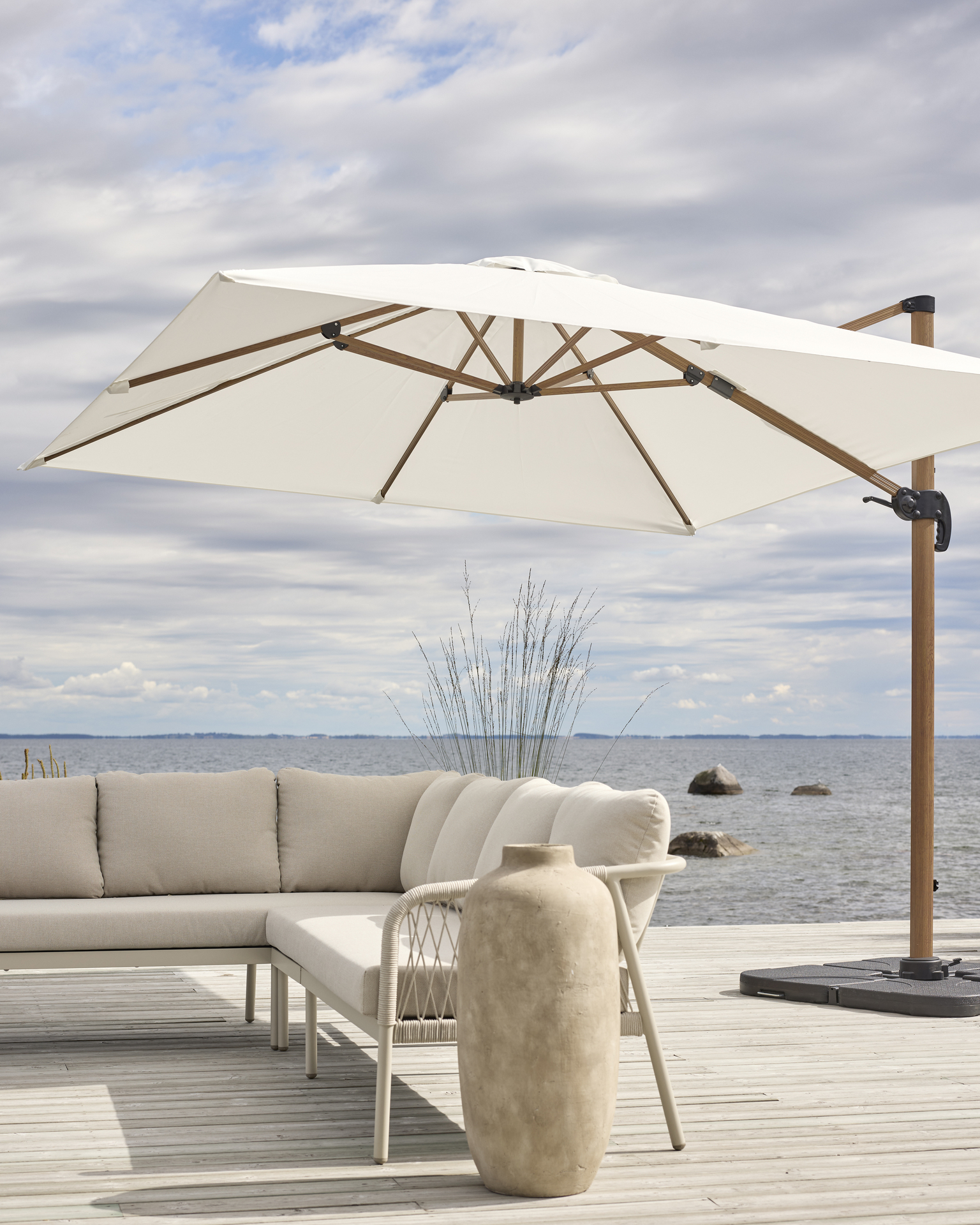 På en altan intill vatten står ett stort vitt parasoll och en beige utesoffa.