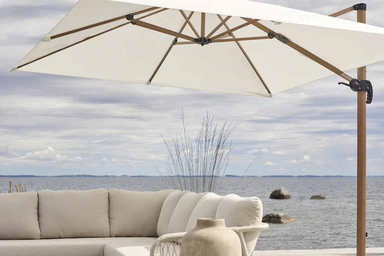 På en altan intill vatten står ett stort vitt parasoll och en beige utesoffa.