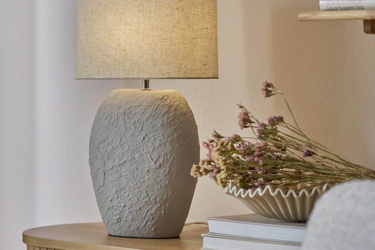 en bordslampa med keramikfot står på en skänk bredvid en skål med torkade blommor