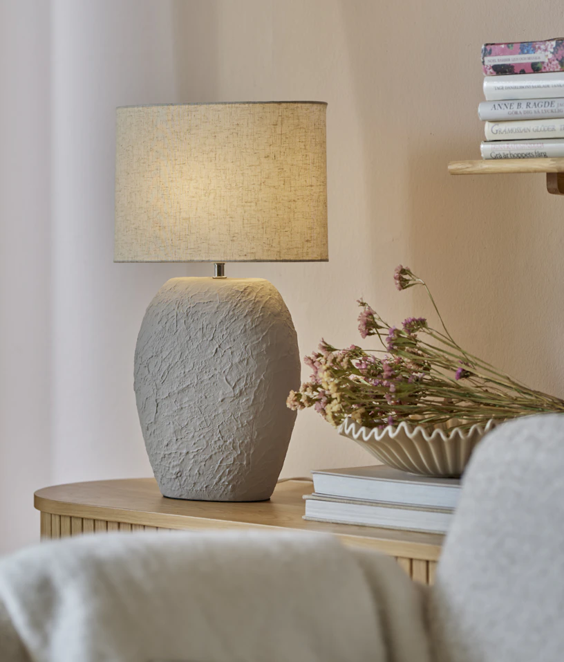 En beige bordslampa står på ett sidobord