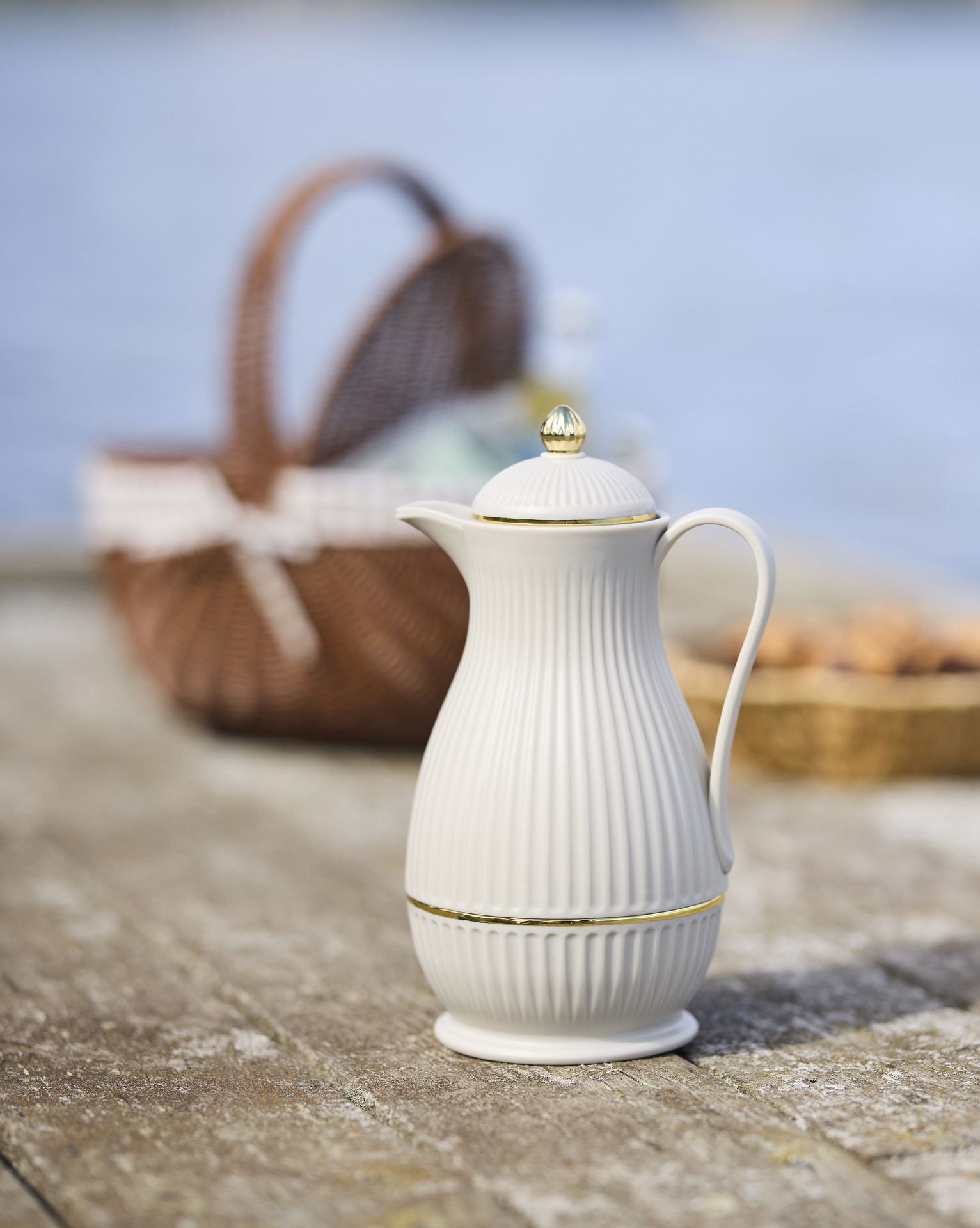 en vit termos står på en brygga framför en picknickkorg och fika