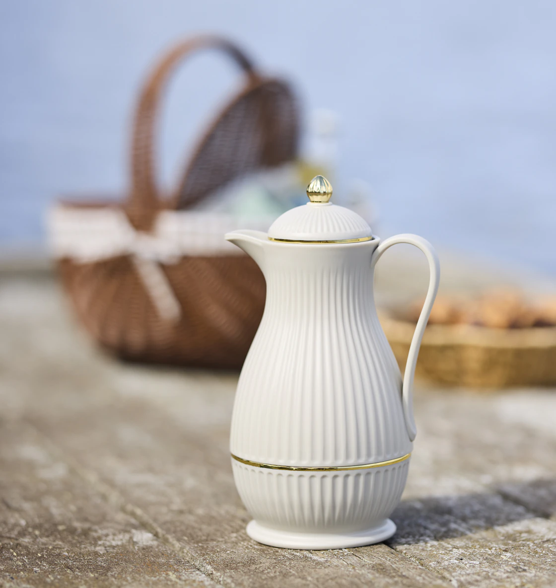 en vit termos står på en brygga framför en picknickkorg och fika