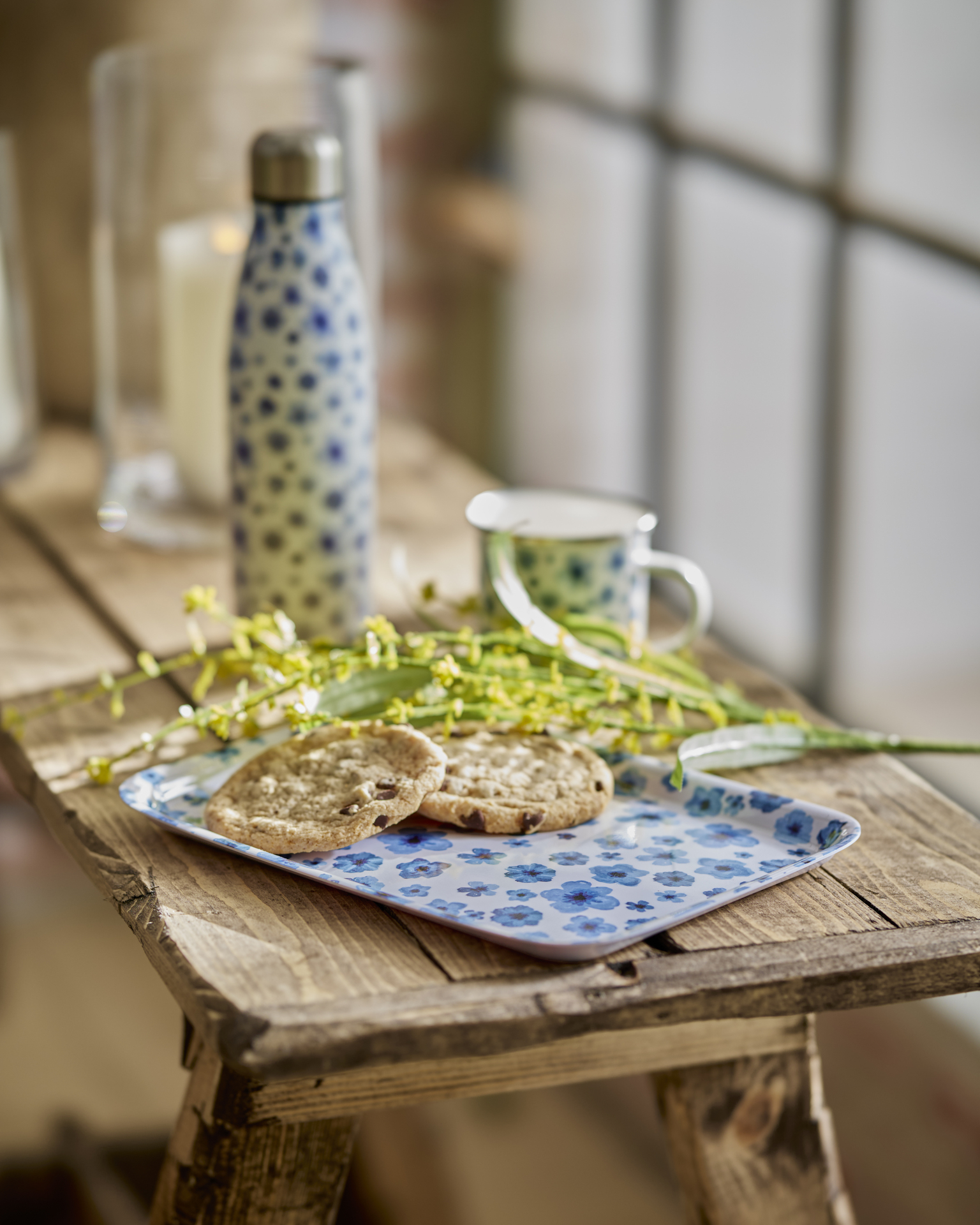 på en träbänk ligger en blåblommig bricka med fika och blommor på