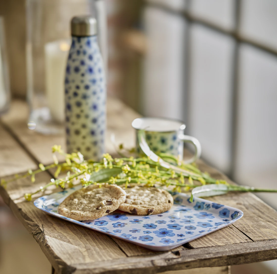 på en träbänk ligger en blåblommig bricka med fika och blommor på