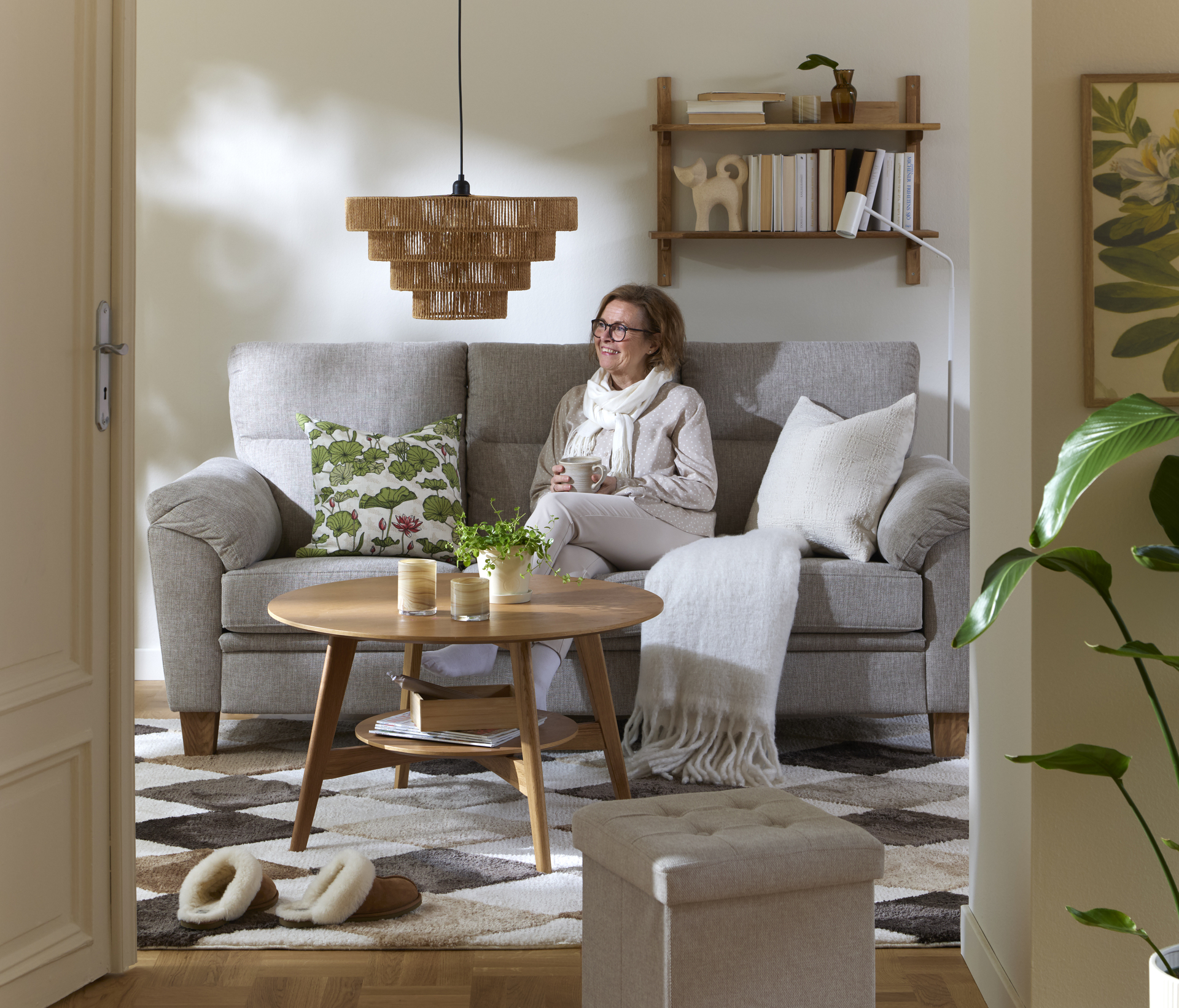 Kvinna sitter i den gråa soffan Tage i ett ljust vardagsrum.