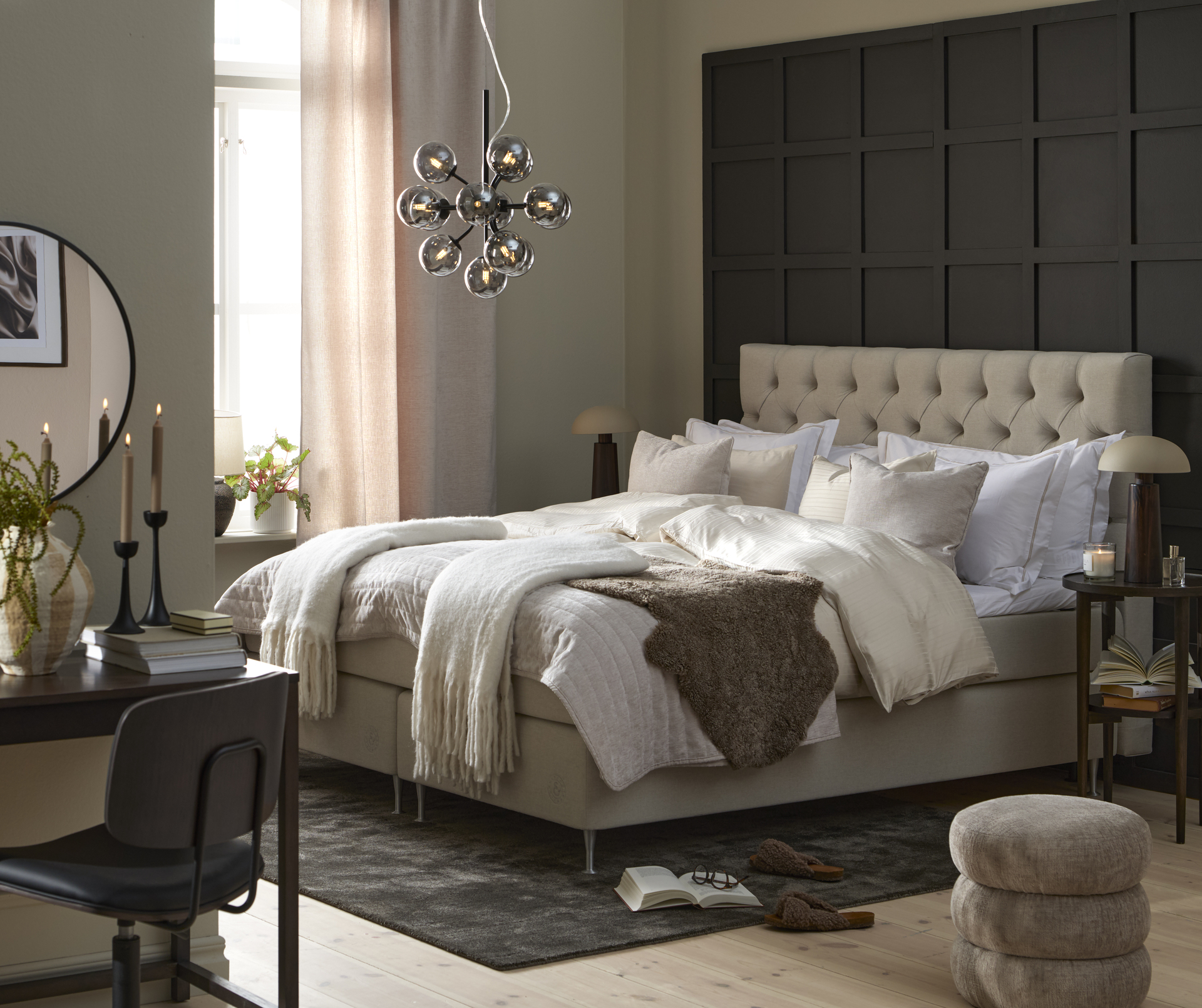 En säng med ljus bäddning och beige pikerad sänggavel står framför en svart vägg i ett sovrum.