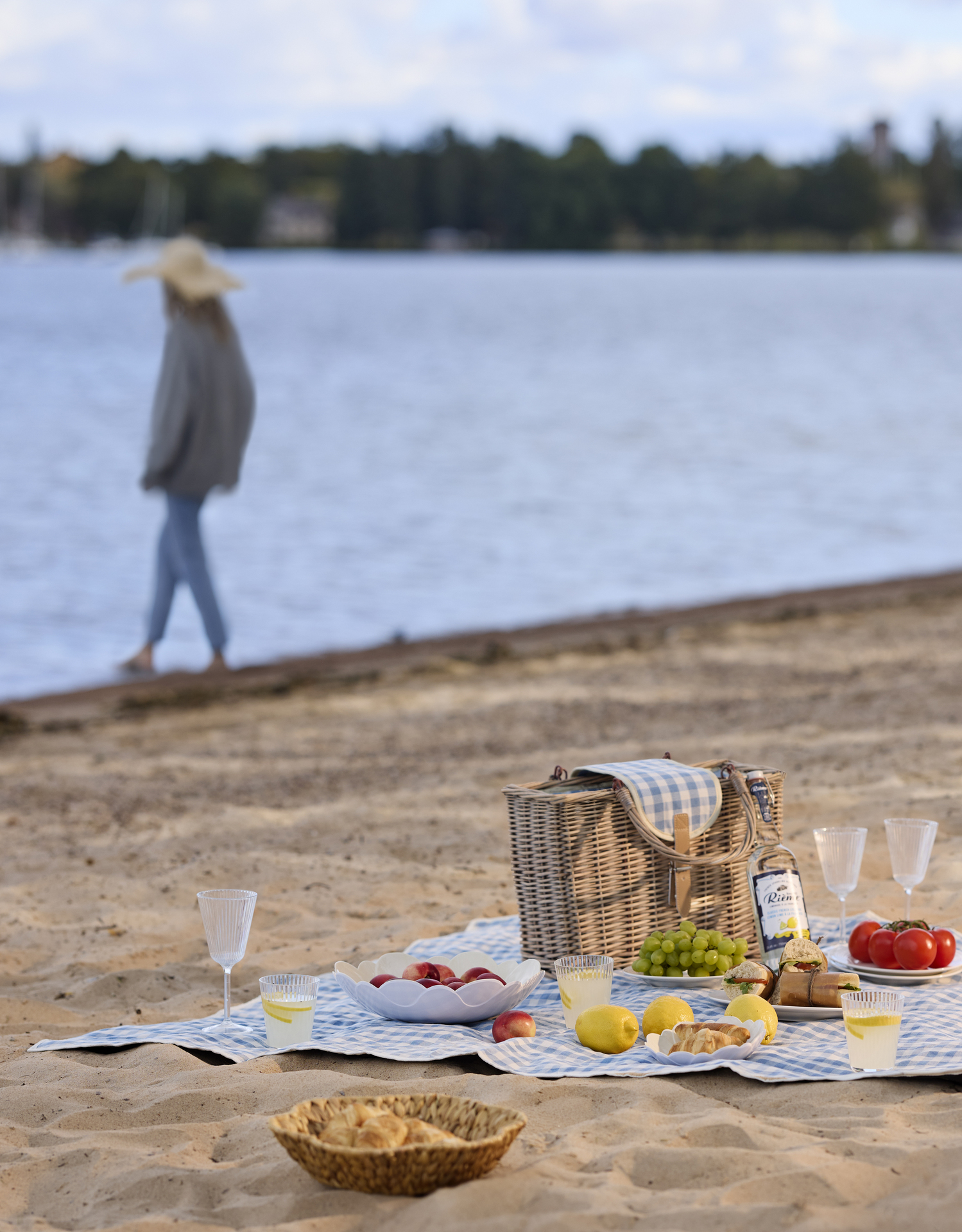 På en strand ligger en blåvit rutig picknickfilt. På filten är en festli picknick framdukad