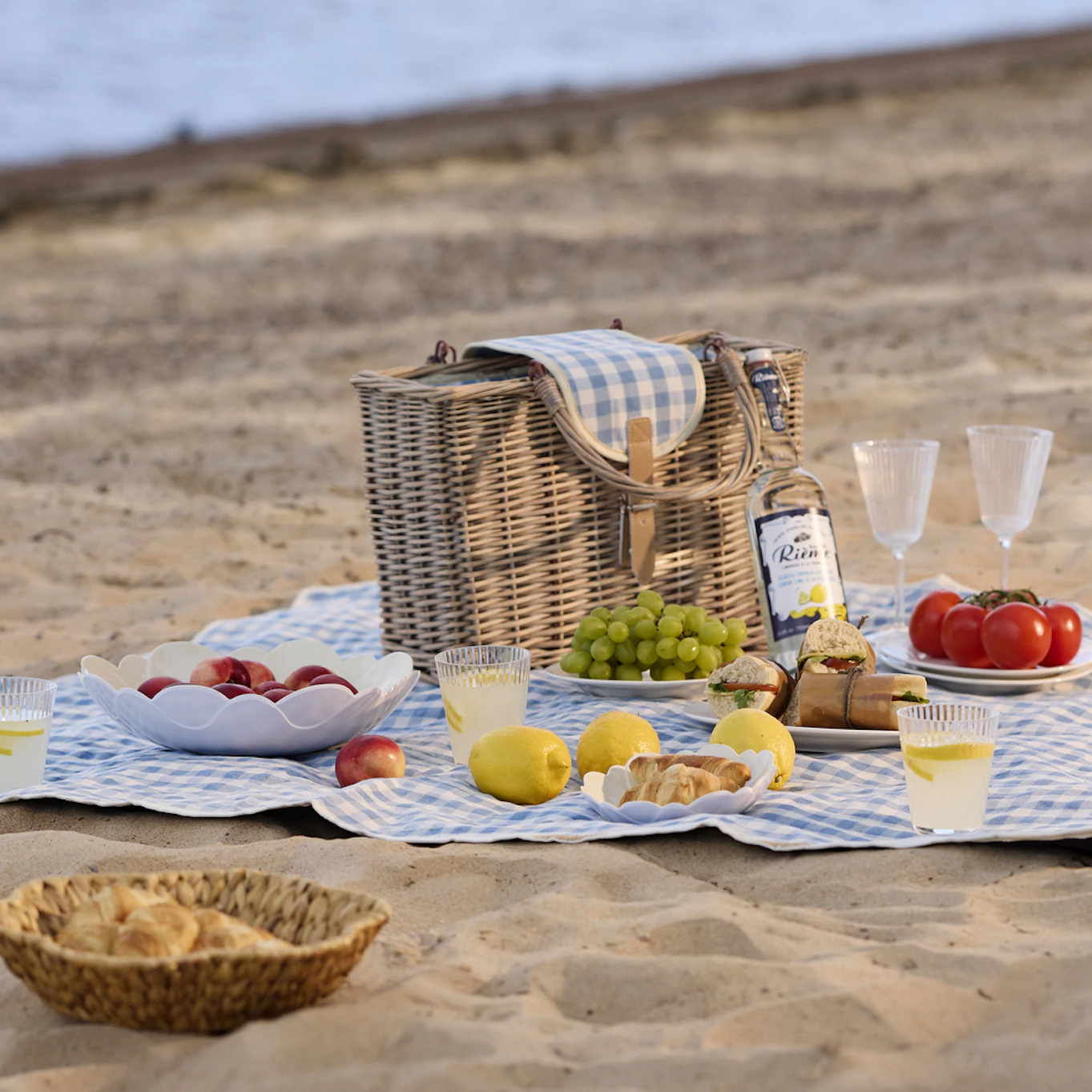 På en strand ligger en blåvit rutig picknickfilt. På filten är en festli picknick framdukad