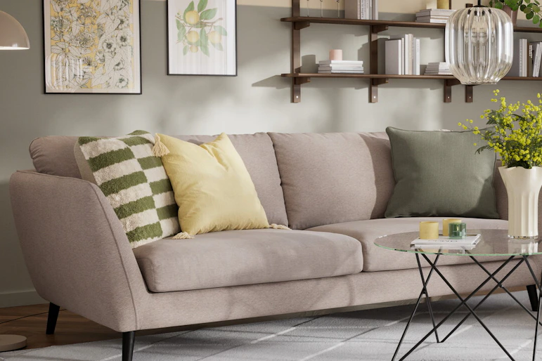 En beige soffa med färgglada kuddar och en grön fåtölj i samma stil står i ett vardagsrum med väggar i grönt och gult.