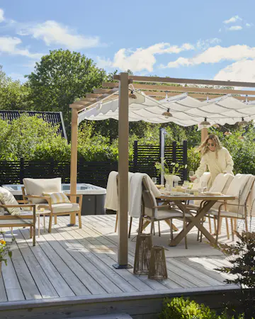 På en solig altan står en kvinna och dukar ett bord under en paviljong