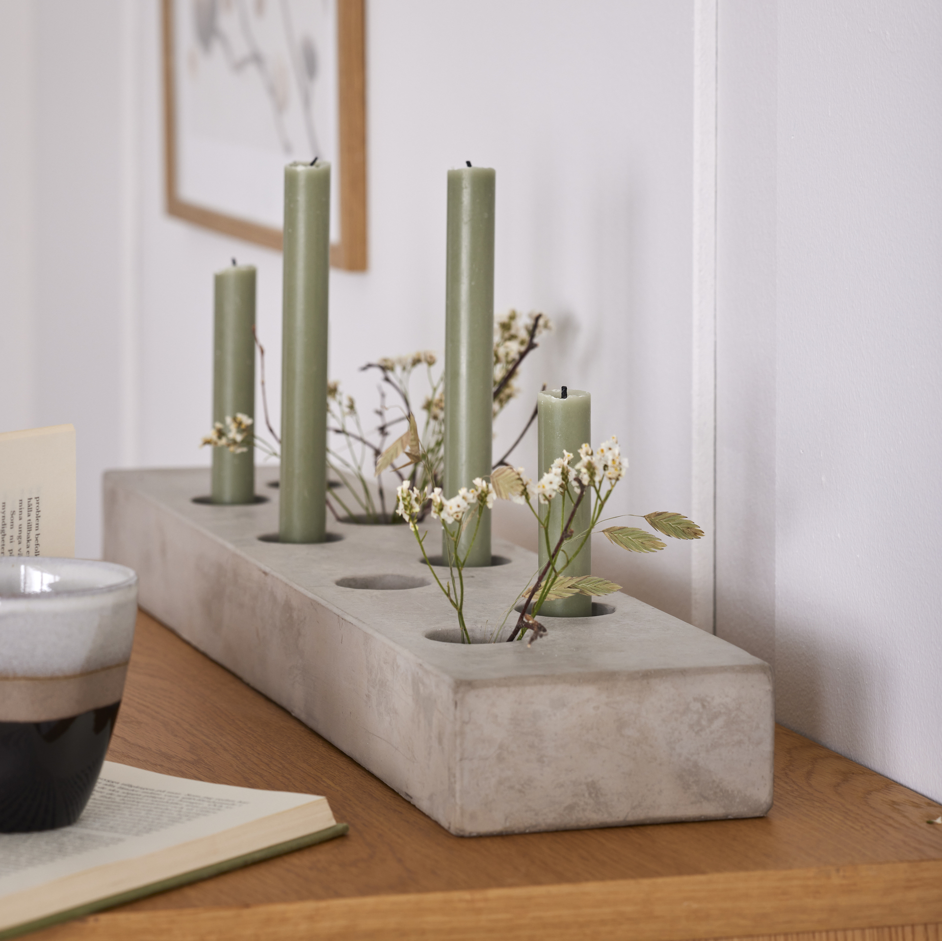 En ljusstake i grå cement har gröna kronljus och blommor i sig.