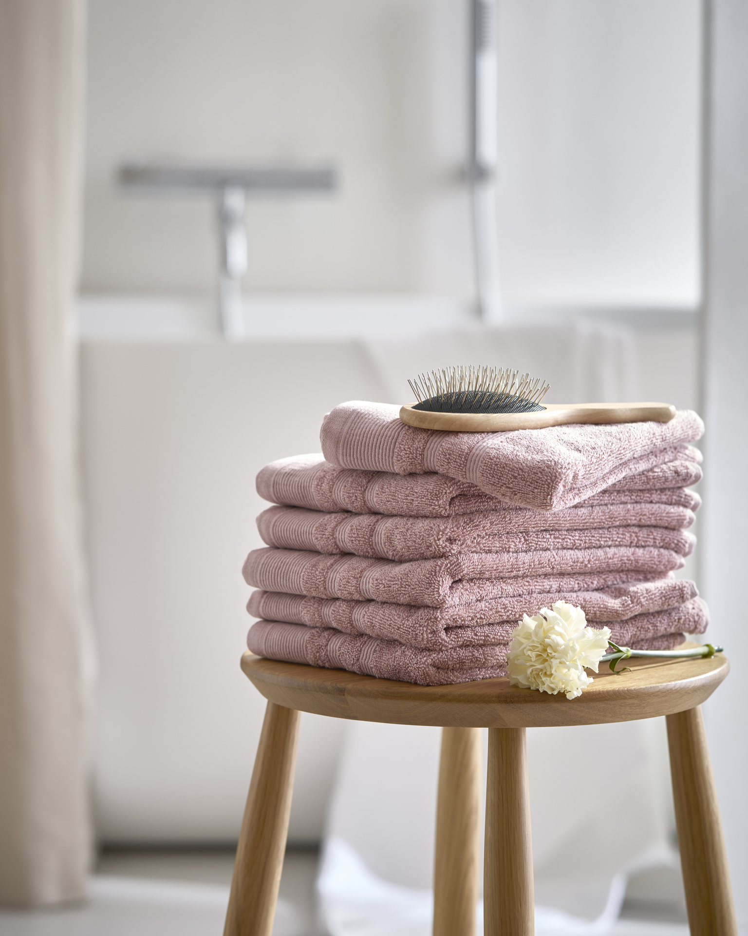 En hög med rosa ihopvikta handdukar liger på en träpall i ett badrum