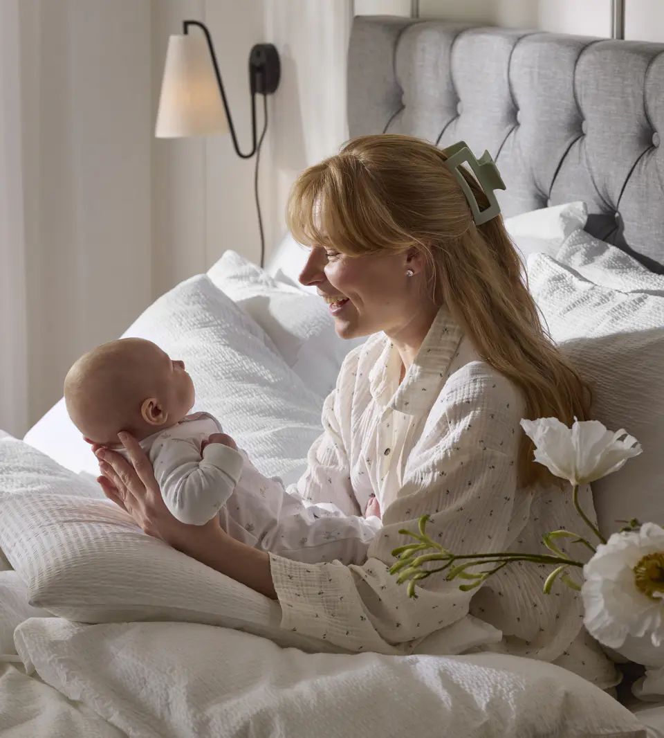 En tjej sitter i en säng och håller i en liten bebis
