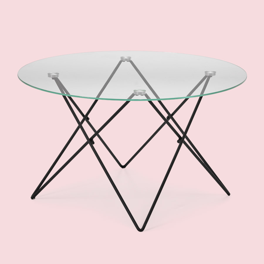Ett modernt runt soffbord med skiva i glas och underrede av metall mot en ljusrosa bakgrund.